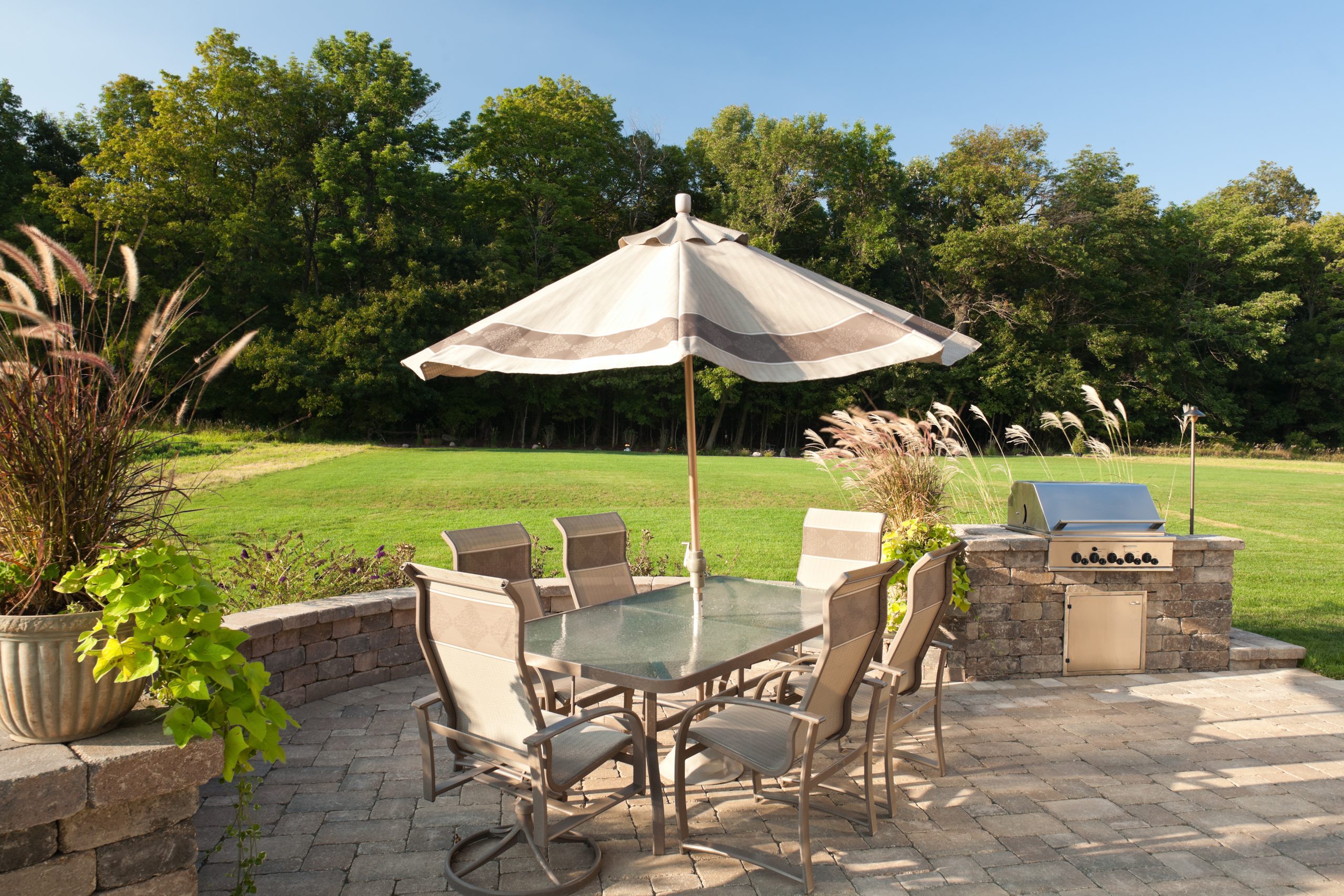 Outdoor living space, patio and chairs with barbeque in a serene summer setting with green grass and blue skies.